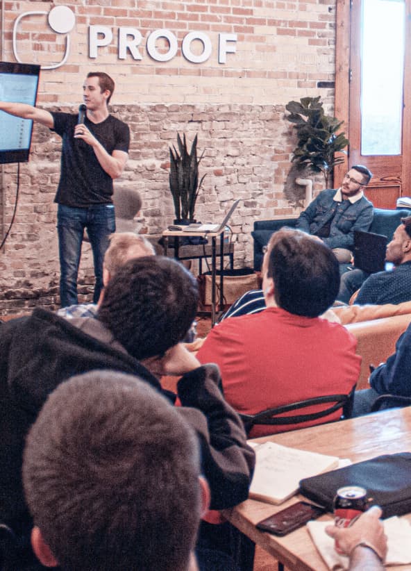 Photo of a presentation in an office showing a person pointing at a screen while others watch